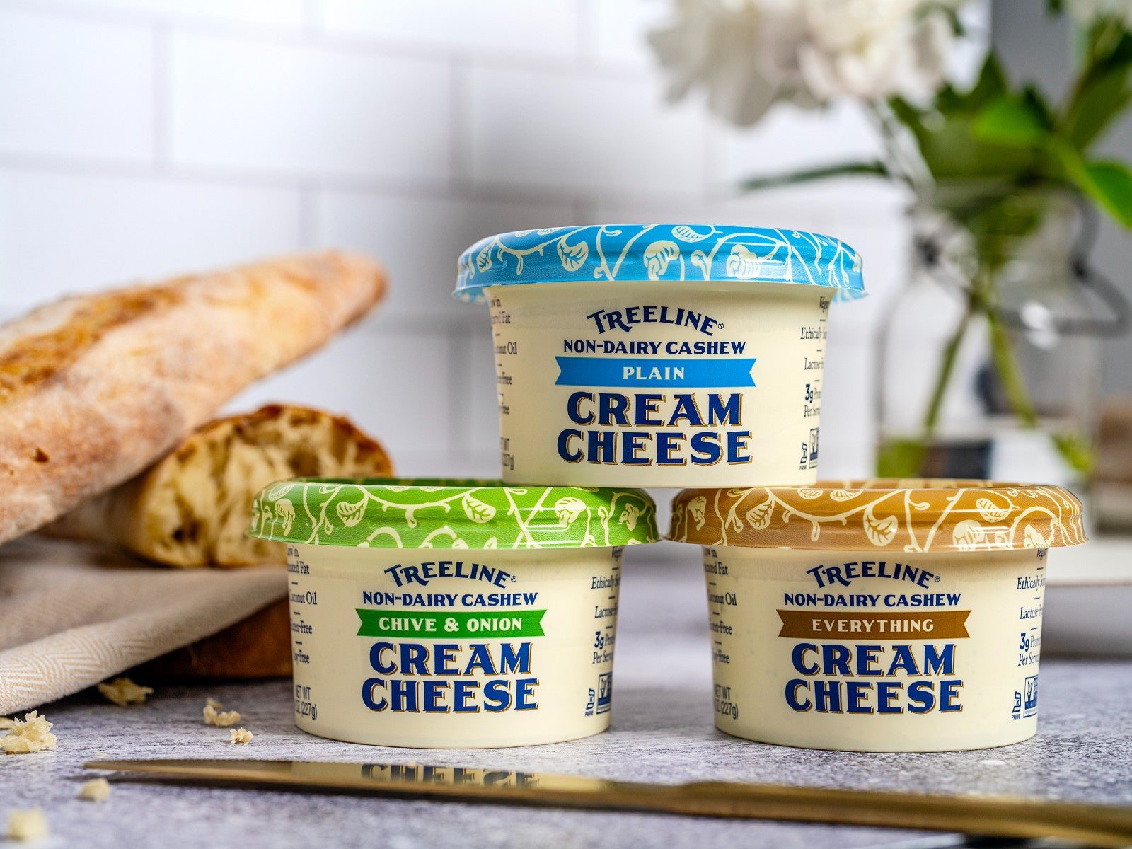 a photo of our 3 vegan cream cheeses stacked in a pyramid on a kitchen counter - plain, chive & onion, everything flavor