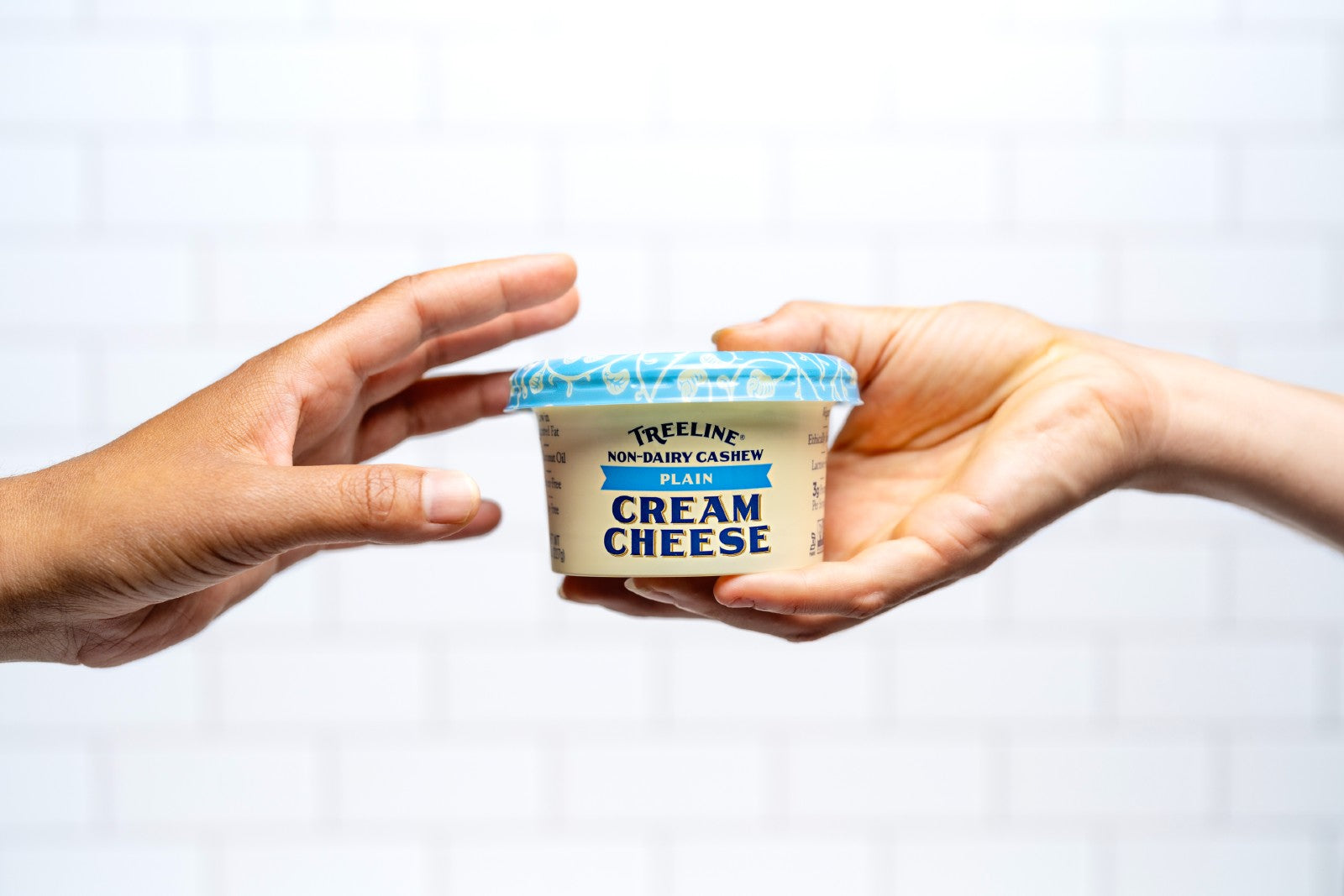 one hand passing a tub of Treeline plain cashew cream cheese to another hand