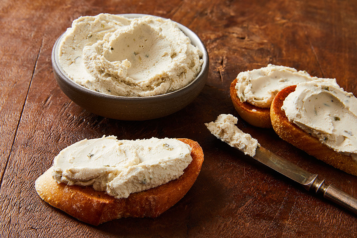 bowl of Treeline vegan soft french-style cheese on  wooden board and spread on toasts