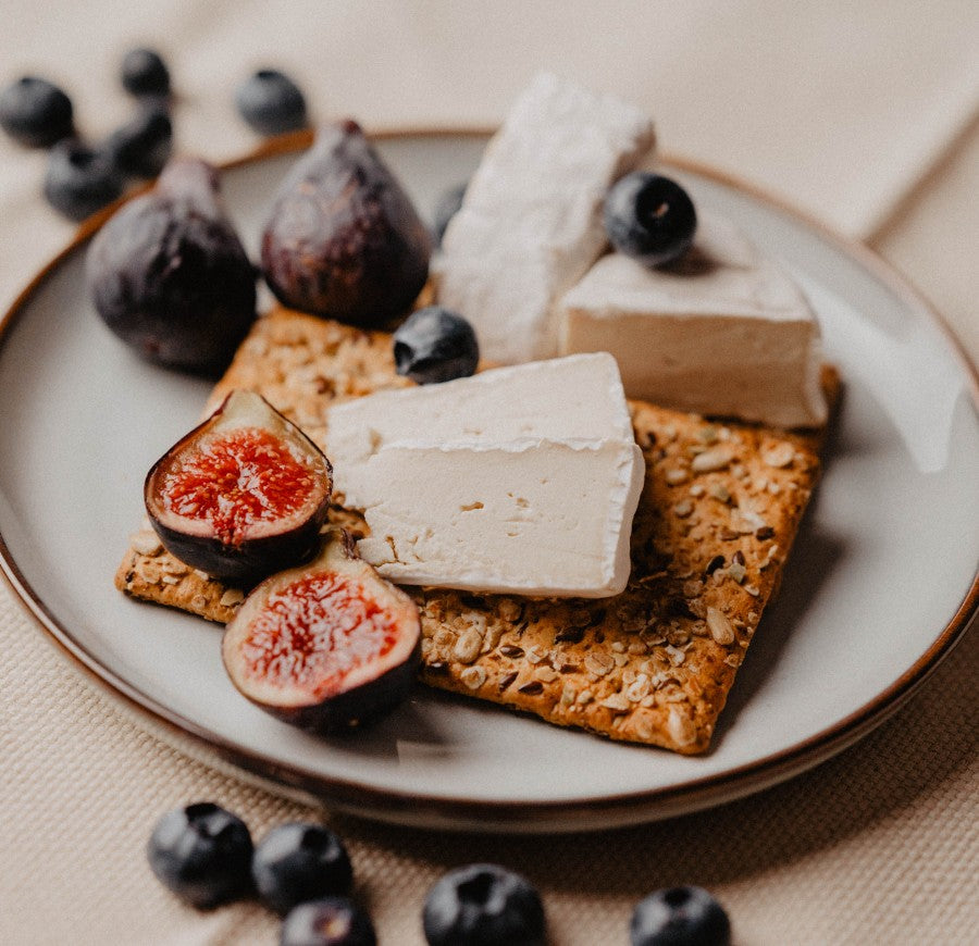 a slice of Treeline vegan bloomy rind cheese on a cracker with some figs and blueberries