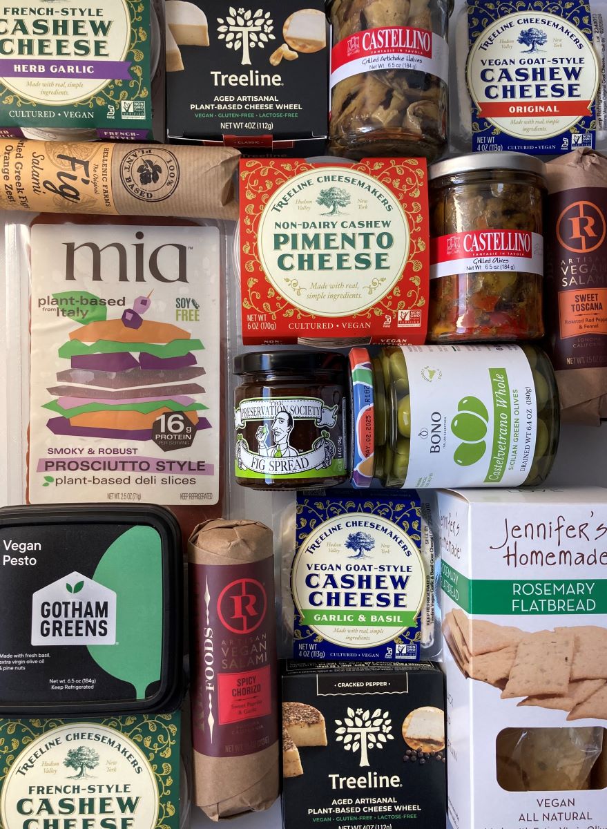 a collection of vegan salami, prosciutto, olives, crackers, and pickles