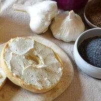 half a bagel spread with Treeline Everything vegan cream cheese, bowls of poppy and caraway seeds, and some garlic