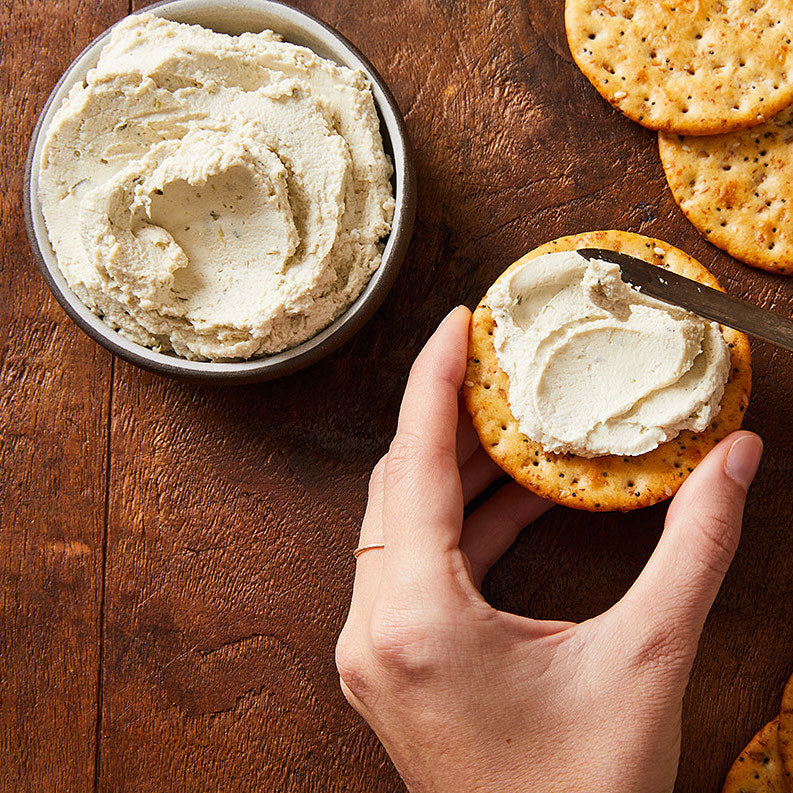 hand spreading vegan cheese on a cracker